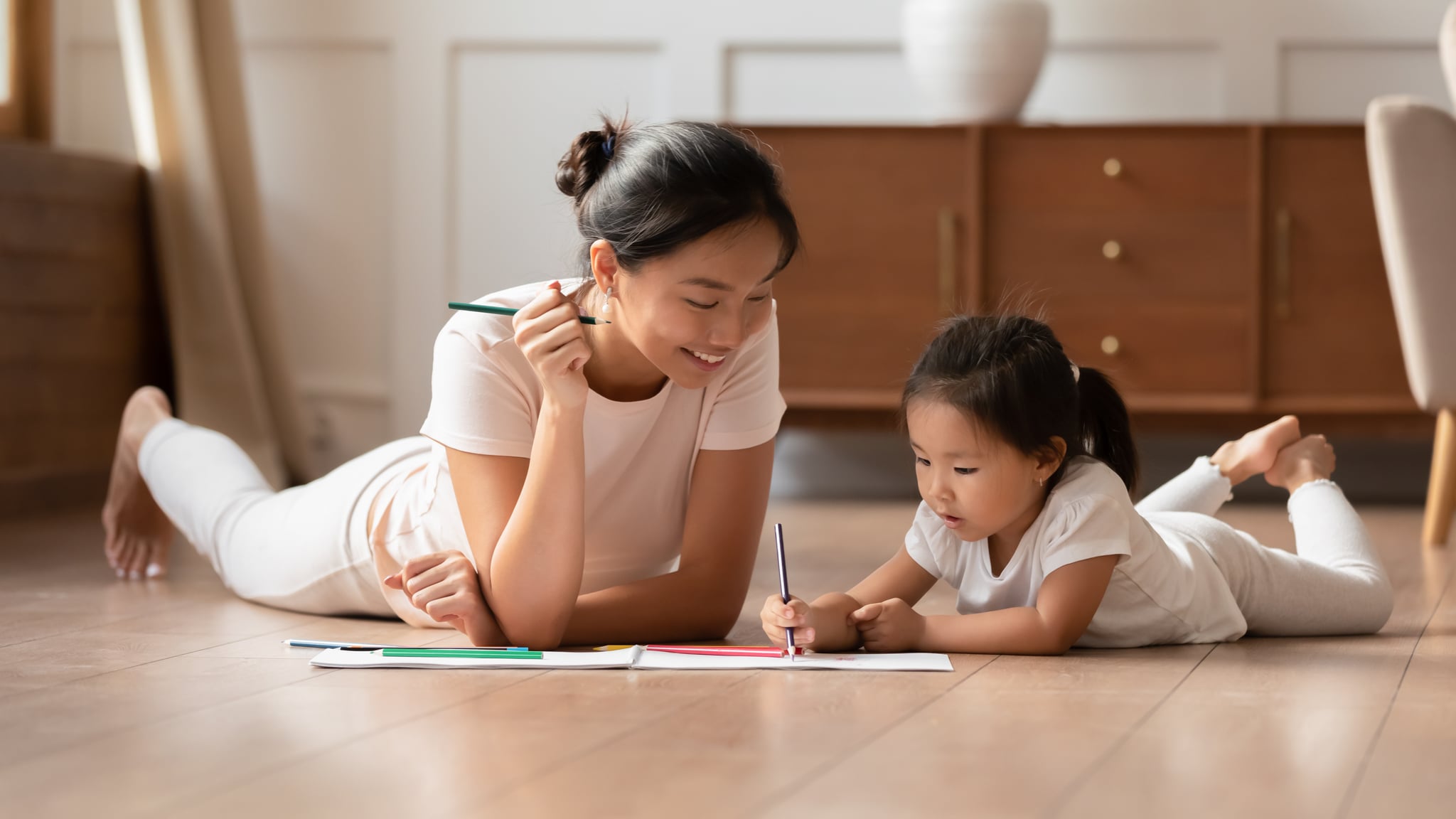 Mother and daughter lying on wooden floor to draw 